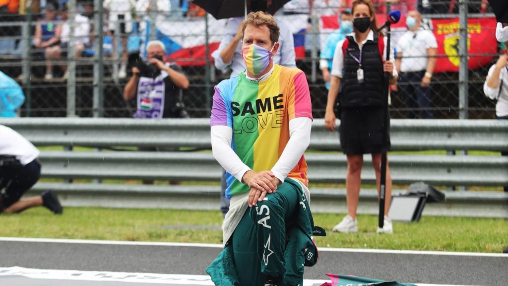 Sebastian Vettel kneeling before the 2021 Hungarian Grand Prix, while wearing a rainbow coloured face mask and a rainbow coloured T-Shirt that says "Same Love". 