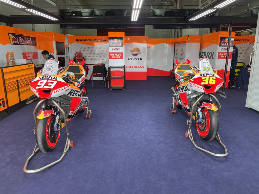 Both Repsol Honda MotoGP bikes parked up in the garage, with both bikes holding "Get Well Soon" messages for their riders.